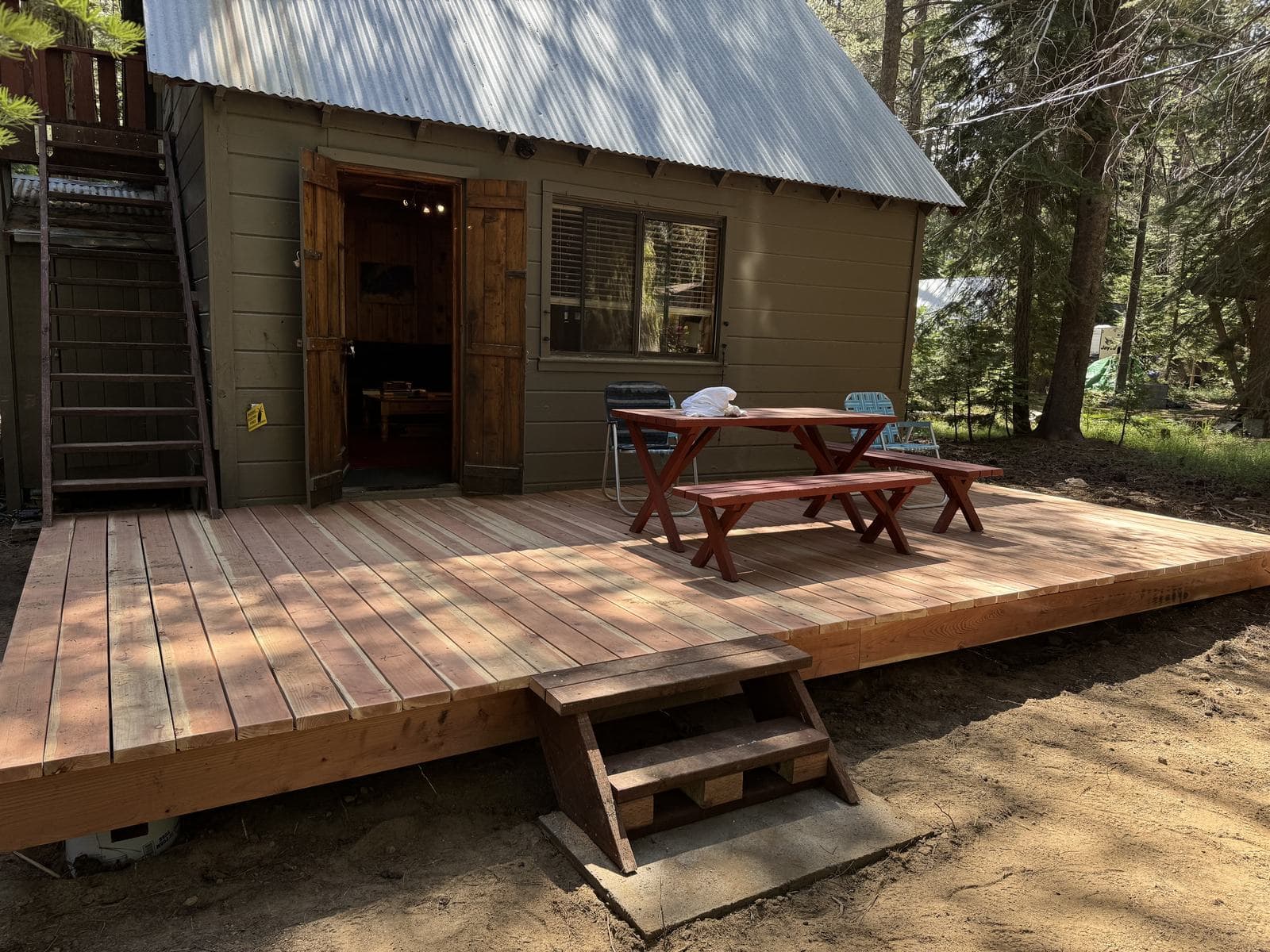 Large ground-level redwood platform deck with a picture-frame border and boxed stair, built across the front of a forest cabin